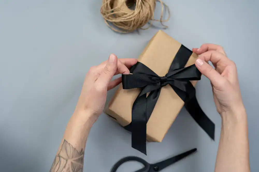 Hands meticulously wrapping a gift box with thick matte paper and twine